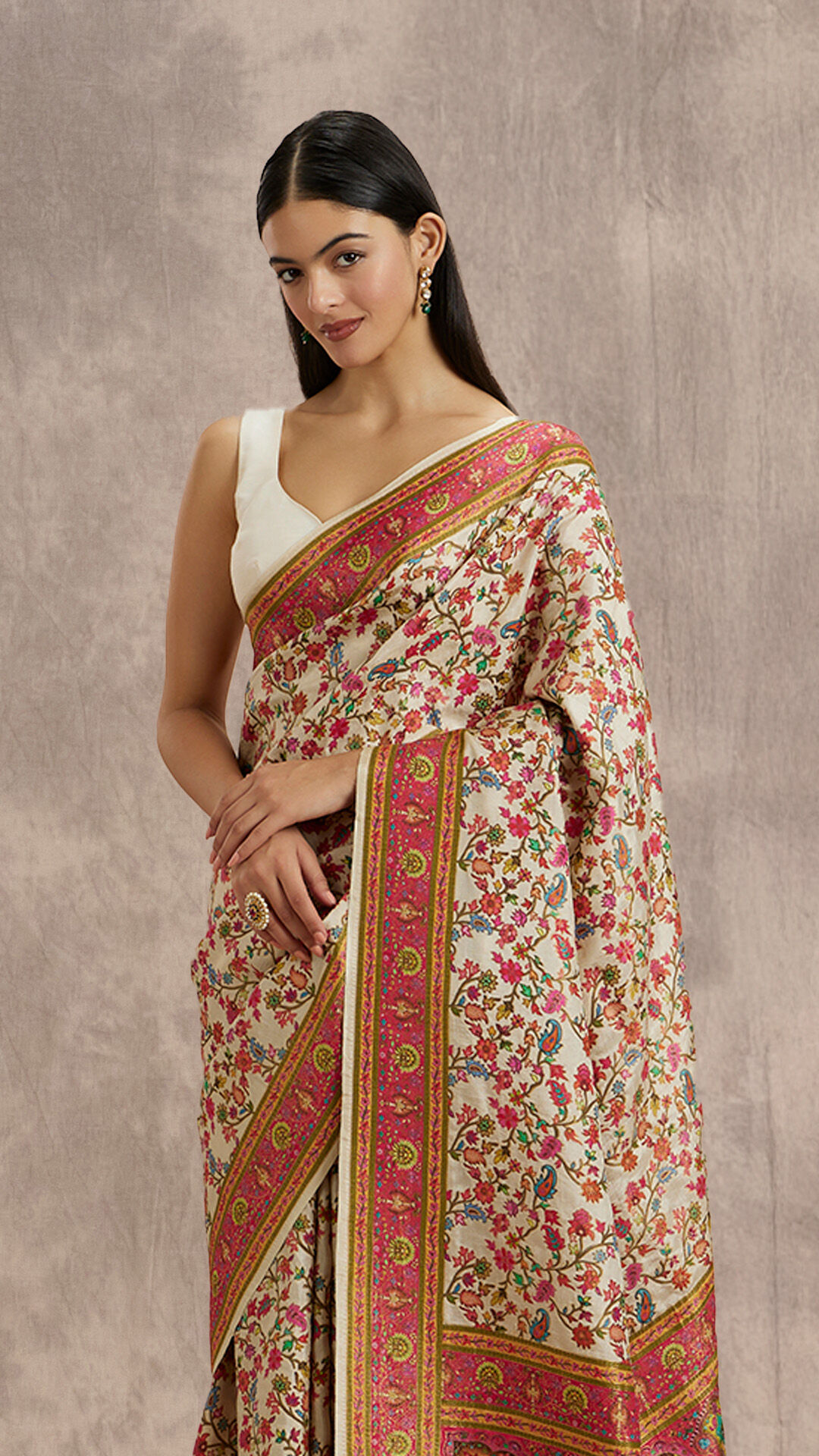 Woman in a stunning cream Parsi Gara or Kashmiri-style silk saree with intricate multicolored floral embroidery and a sleeveless white blouse.